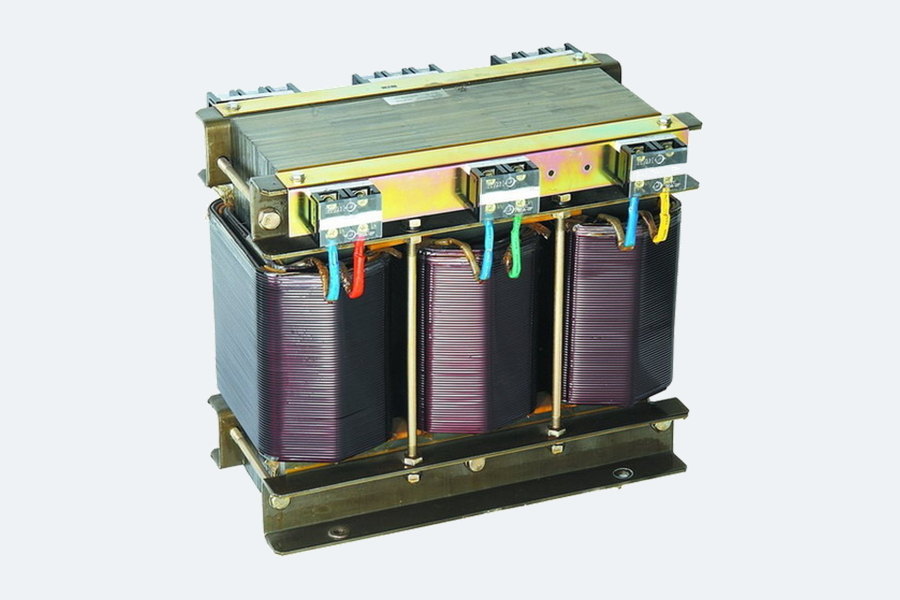 A three-phase isolation transformer: copper windings on a laminated steel core with terminal bars along the top and colour-coded tails.
