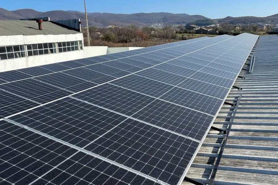 A long run of photovoltaic modules mounted in rows across an industrial shed roof under a clear sky.